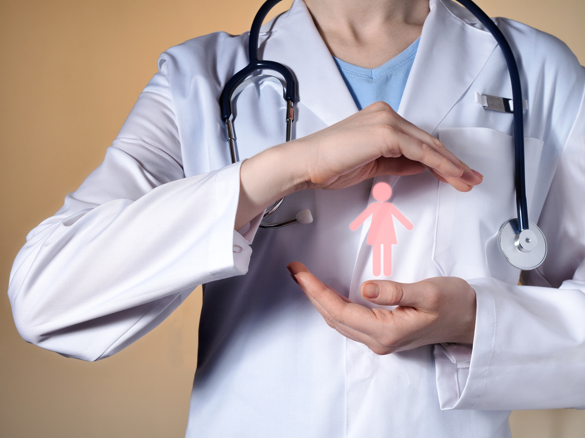 A woman doctor holds a woman's pictograph in her hands. Female doctor with a stethoscope gesticulating on a beige background.