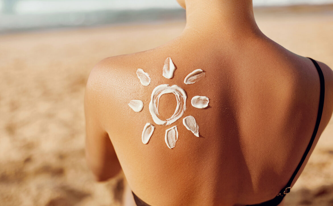 Skin care. Sun protection. Woman apply sun cream. Woman With Suntan Lotion On Beach In Form Of The Sun. Portrait Of Female With  Drawn Sun On A Shoulder. Suncream. Girl Holding Moisturizing Sunblock.