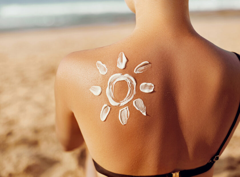 Skin care. Sun protection. Woman apply sun cream. Woman With Suntan Lotion On Beach In Form Of The Sun. Portrait Of Female With  Drawn Sun On A Shoulder. Suncream. Girl Holding Moisturizing Sunblock.