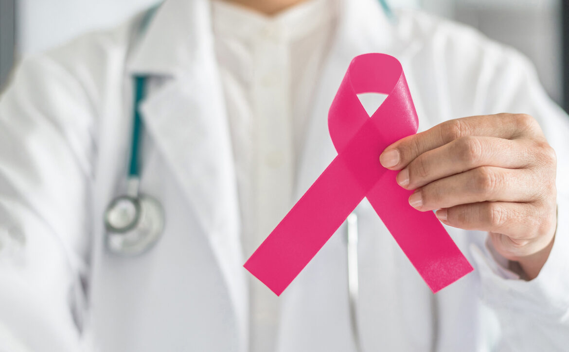 Pink ribbon for breast cancer awareness in doctor's hand, symbolic bow color for raising awareness campaign on women (female)  patient living with breast tumor illness