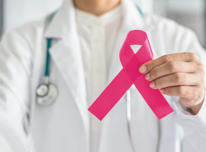 Pink ribbon for breast cancer awareness in doctor's hand, symbolic bow color for raising awareness campaign on women (female)  patient living with breast tumor illness