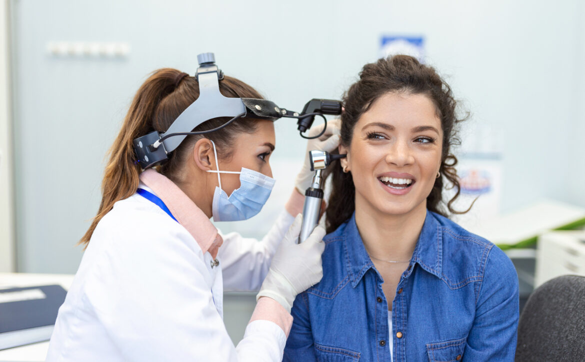 Hearing exam. Otolaryngologist doctor checking woman's ear using otoscope or auriscope at medical clinic. Otorhinolaryngologist pulling ear with hand and looking at it with otoscope closeup.