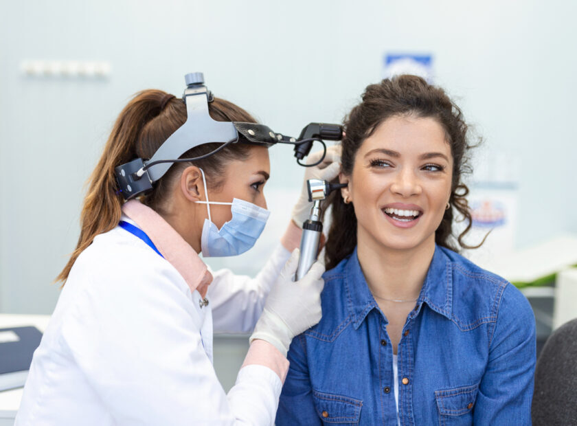 Hearing exam. Otolaryngologist doctor checking woman's ear using otoscope or auriscope at medical clinic. Otorhinolaryngologist pulling ear with hand and looking at it with otoscope closeup.