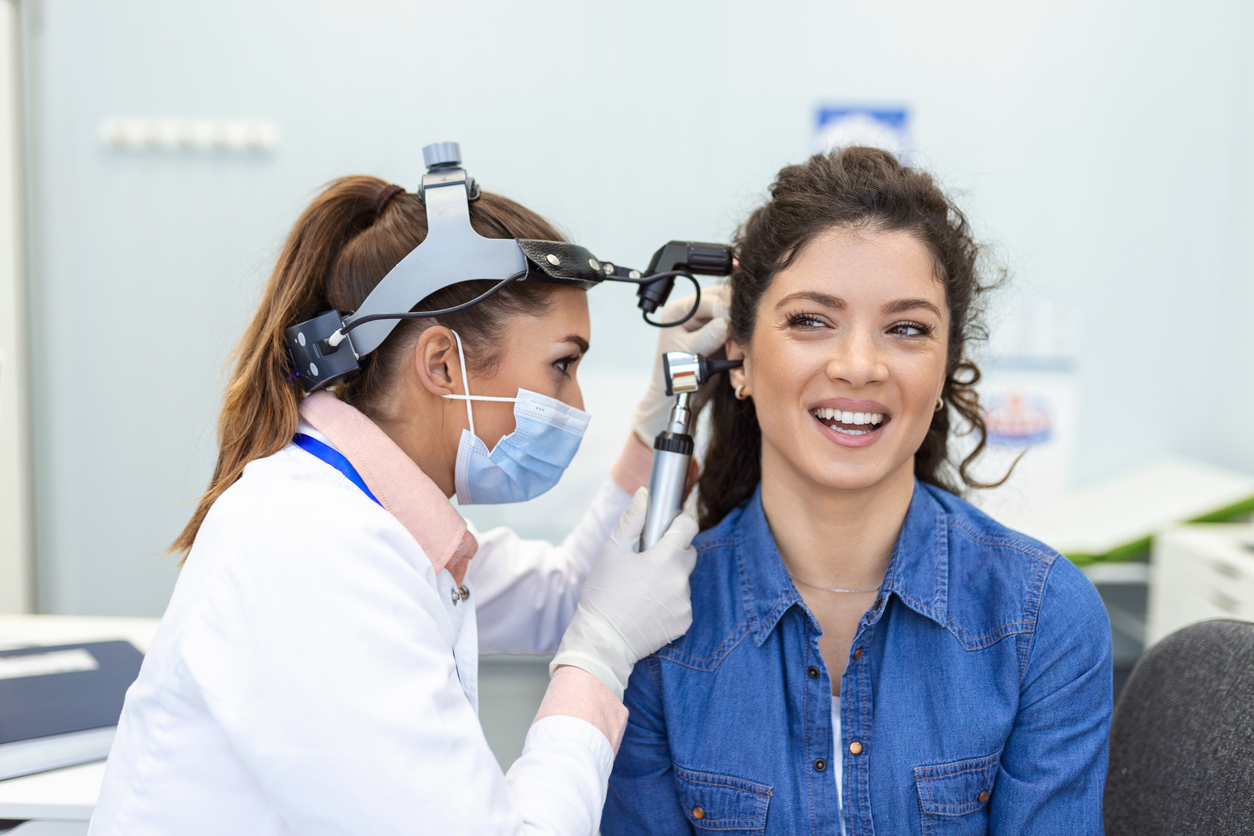 Hearing exam. Otolaryngologist doctor checking woman's ear using otoscope or auriscope at medical clinic. Otorhinolaryngologist pulling ear with hand and looking at it with otoscope closeup.